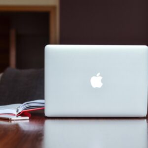 A clean and modern workspace featuring a laptop, book, and smartphone on a wooden table.