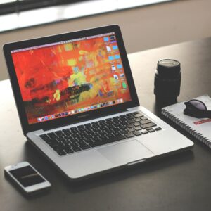 A clean, organized workspace featuring a MacBook, smartphone, and notebook.